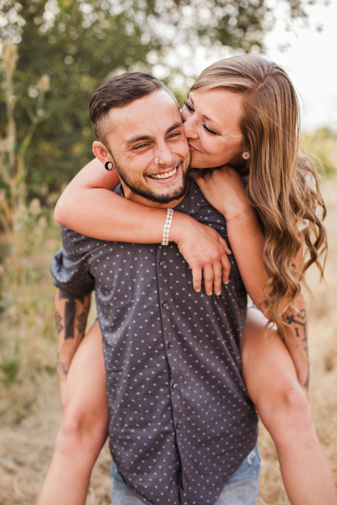 woman on man's back laughing and kissing his cheek