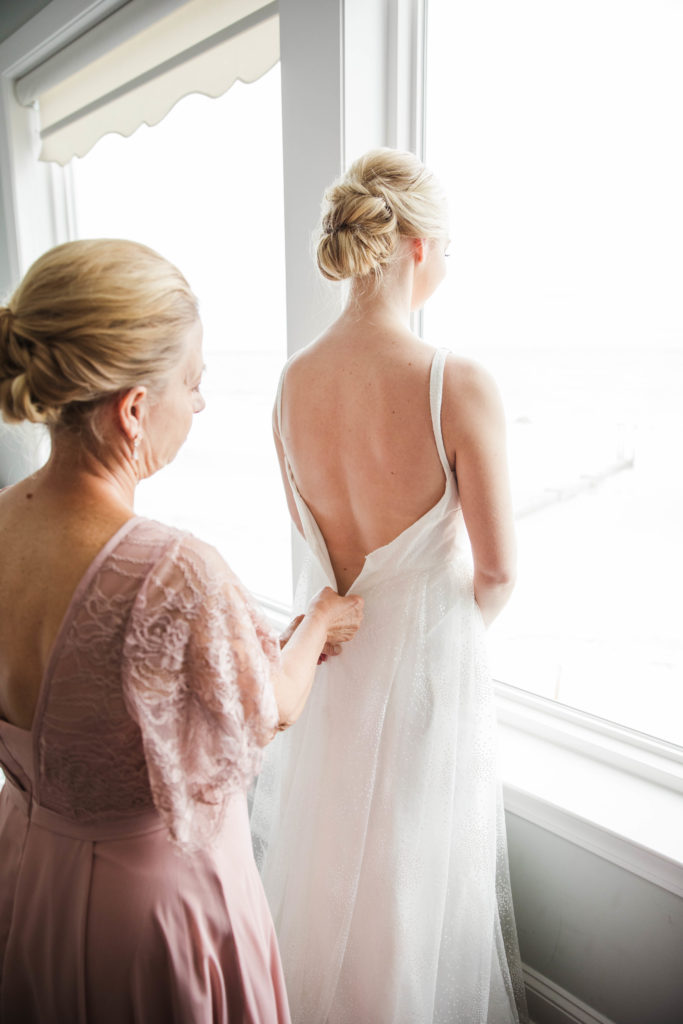 bride in window getting dress zipped up before ceremony