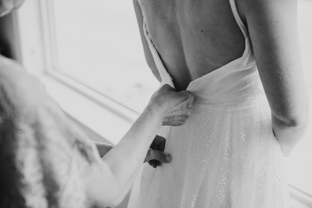bride getting dressed in her wedding gown while mom zips her up