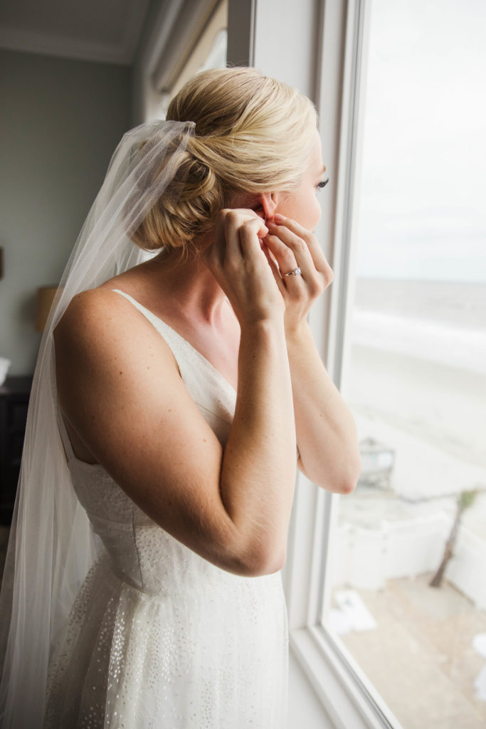 bride putting earrings on while wearing wedding dress and veil before ceremony
