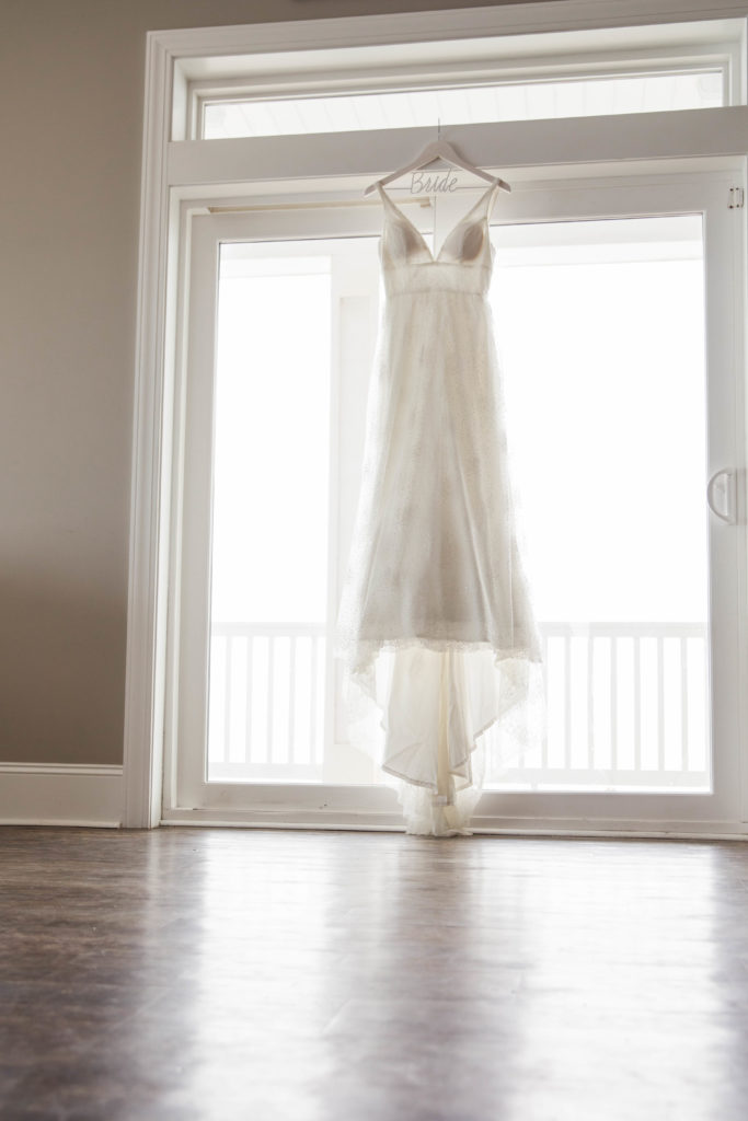 detail shot of wedding dress hanging in window on customized 'bride' hanger at beach wedding
