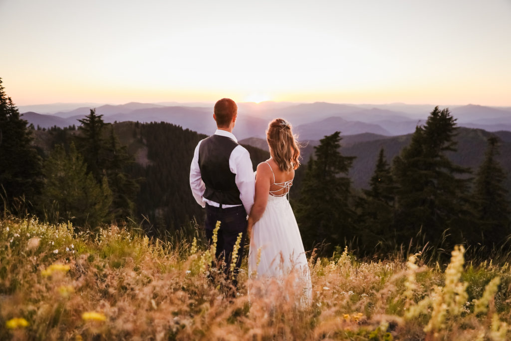bride and groom holding hands and looking off into sunset after mountain top elopement