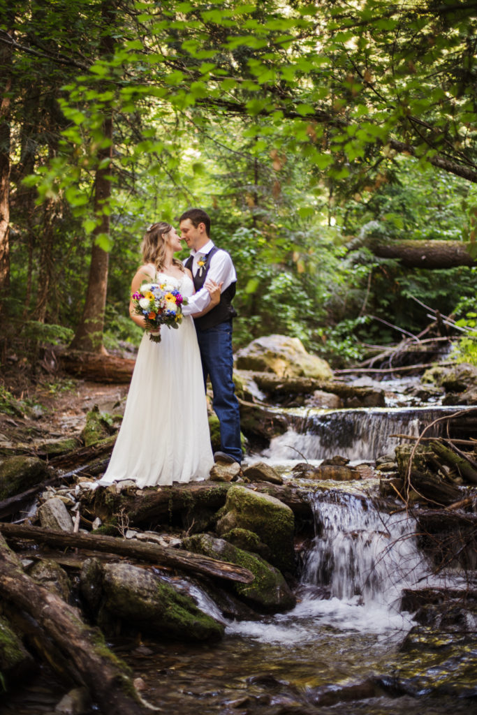bride and groom kissing on waterfall in wallace idaho. Bride wears lacy gown, and groom wearing brown vest