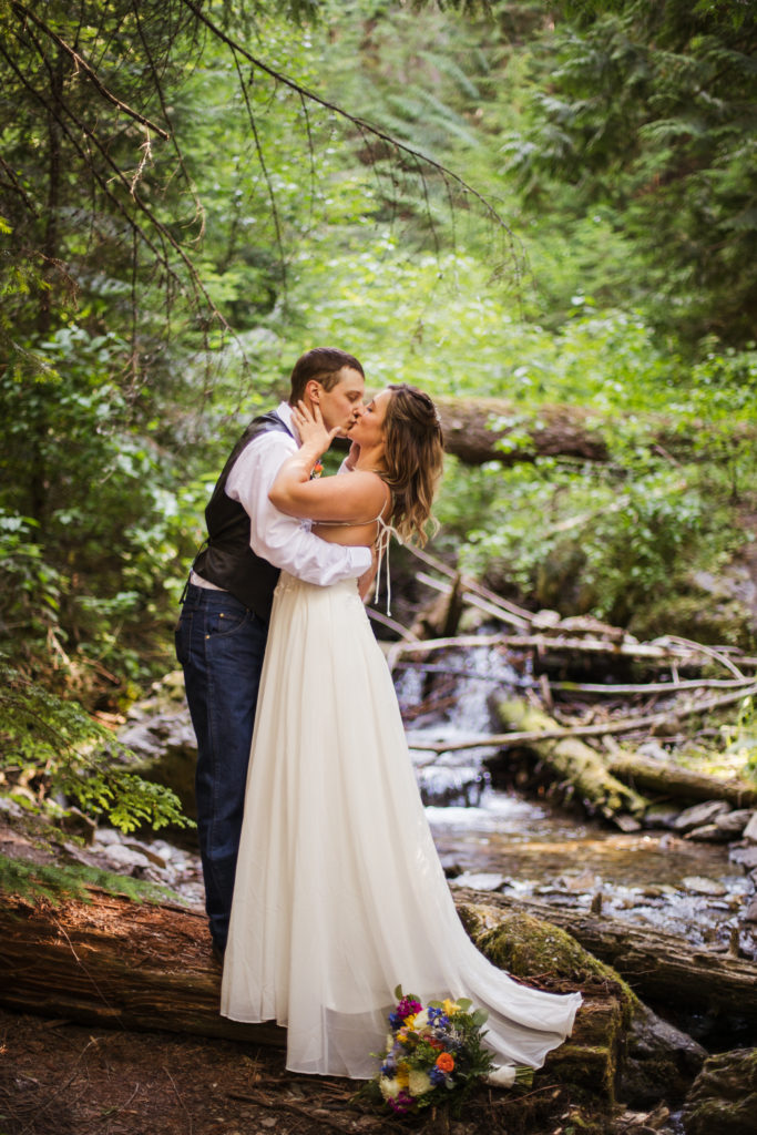 bride and groom embrace after mountain top elopement while wearing wedding gown and groom in white shirt and vest