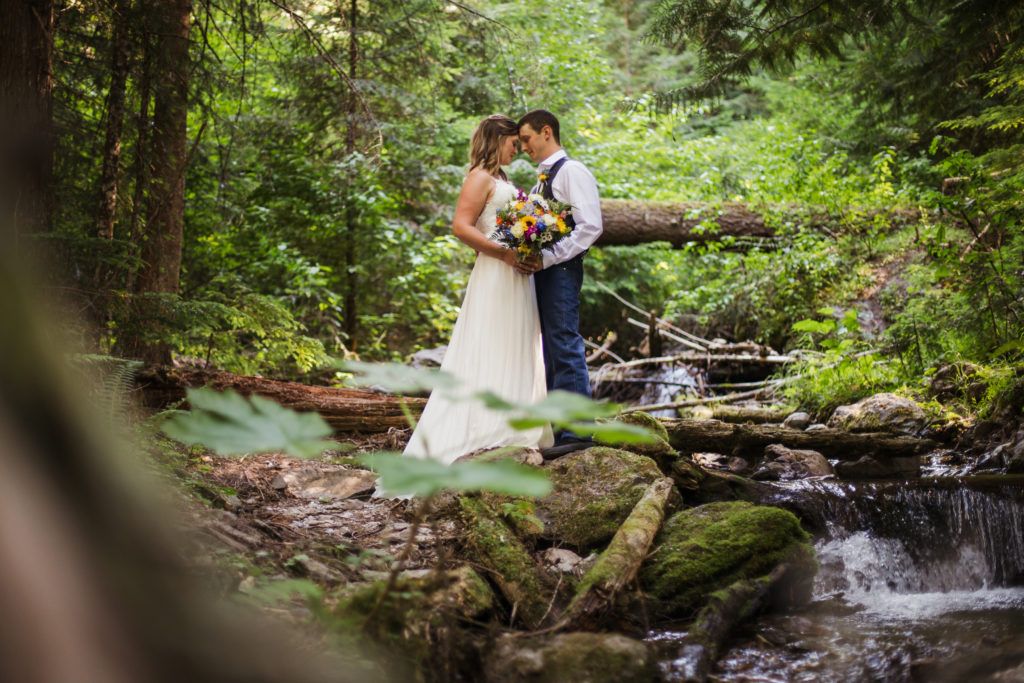 bride and groom kissing at waterfall after mountain top elopement