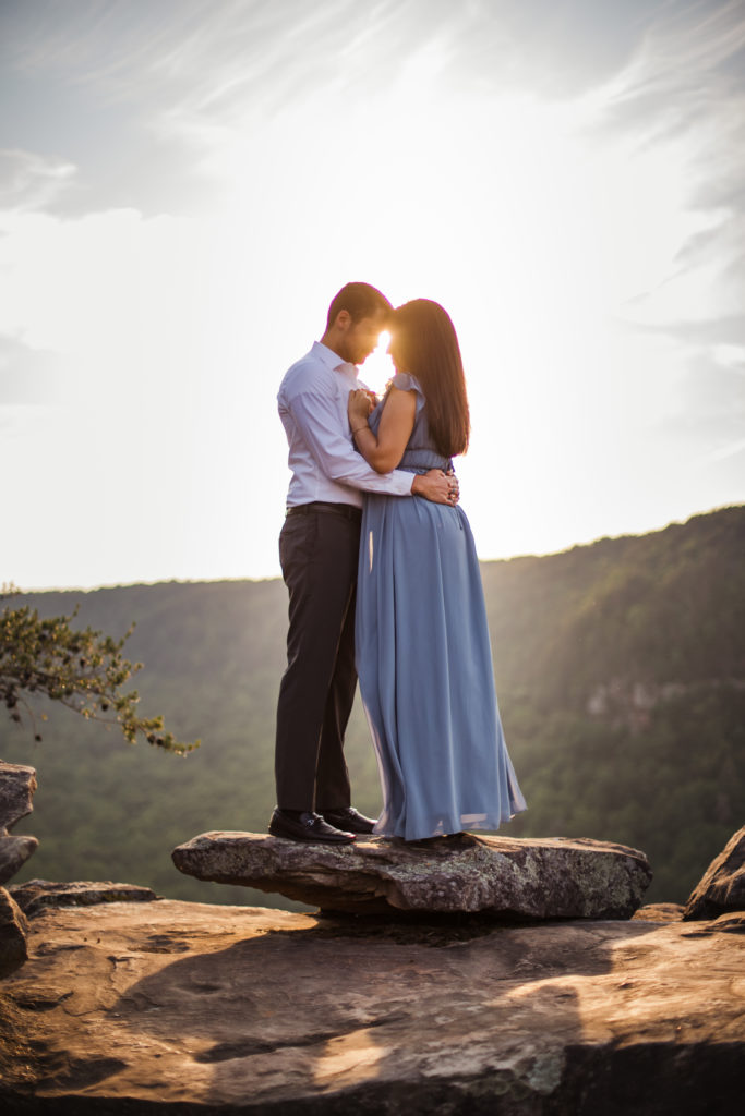 man and woman hugging on mountain top during sunset engagement session