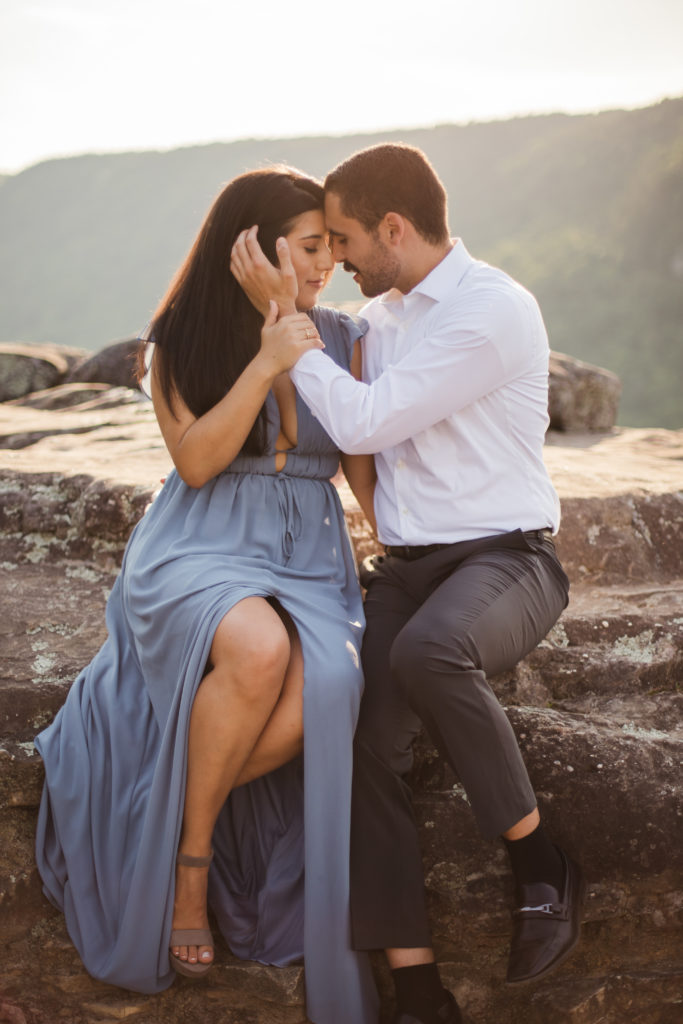 man and woman embracing while sitting on rock during engagement session