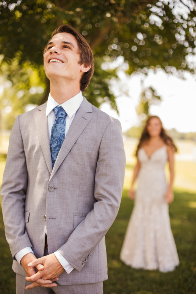 bride walking up to groom, and groom smiling on wedding day
