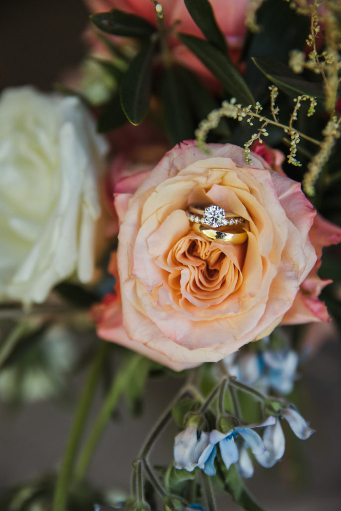detail shot of wedding rings in bridal bouquet of peach roses