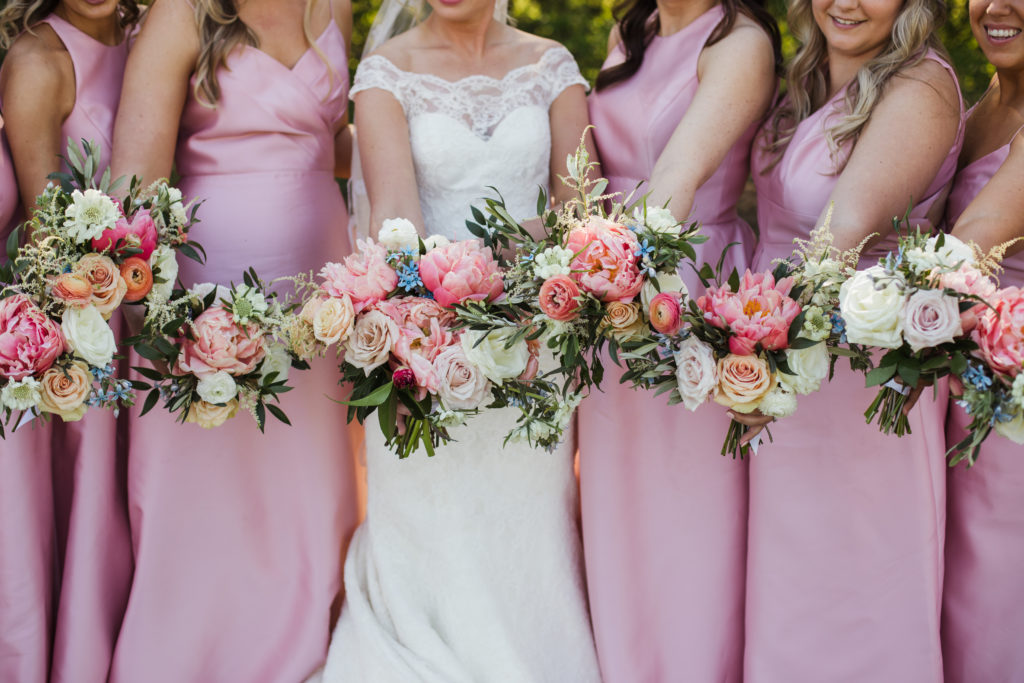 bride and bridesmaids holding bouquets of pink, white, and coral florals together