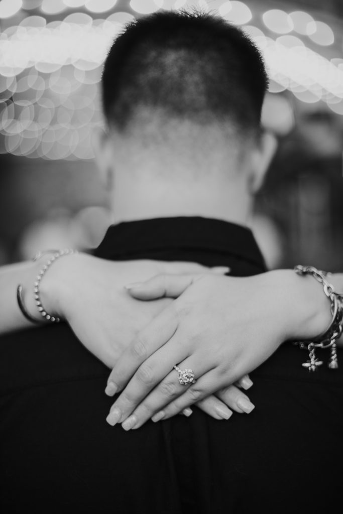 man and woman hugging with woman's hands around man's neck showing off engagement ring