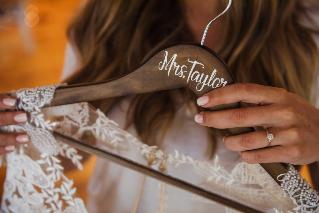 bride holding wooden hanger with wedding dress on it