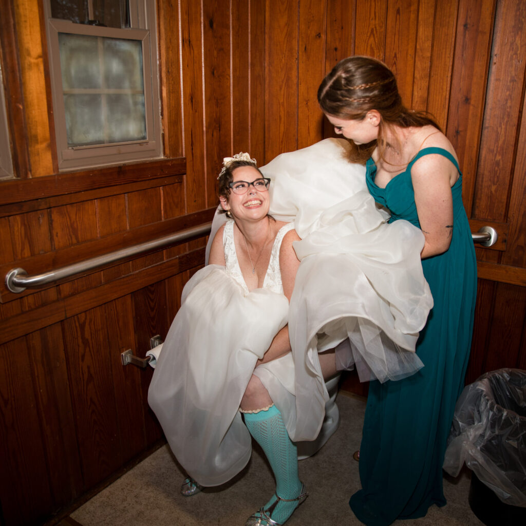Bride using the restroom with bridesmaid holding her dress